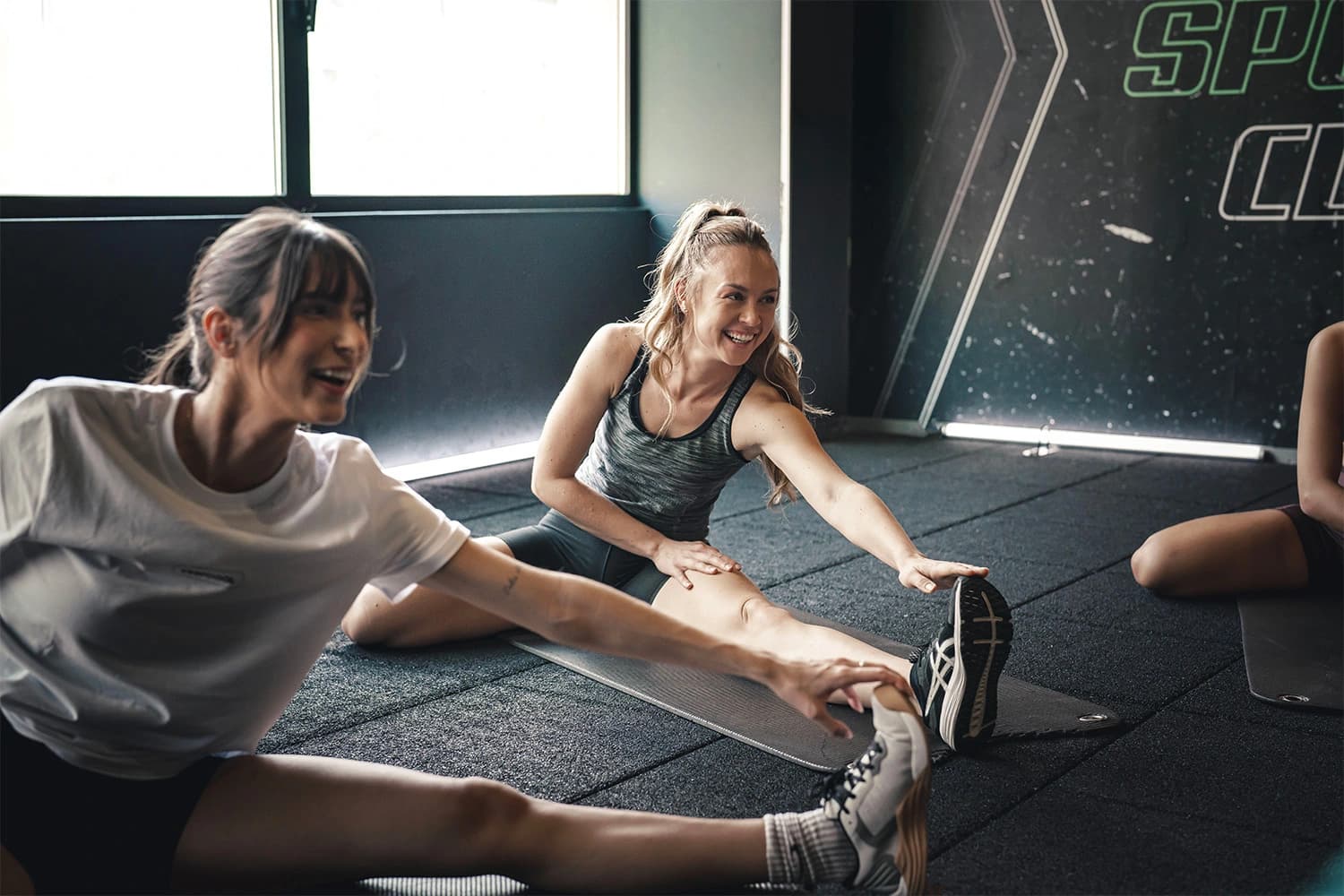 Deux femmes font un exercice d'étirement dynamique dans une salle de sport moderne, cours collectifs fitness.
